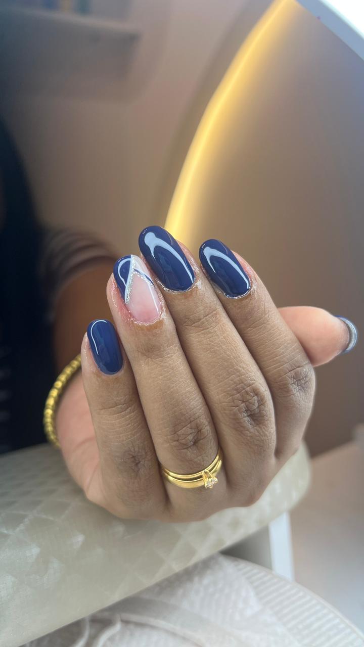 Unhas alongadas azul escuro com brilho intenso e detalhe decorado em uma das unhas.